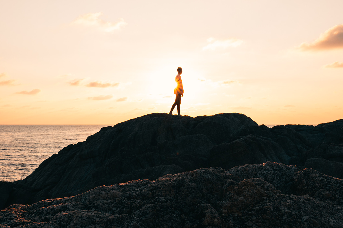 Quiet Answers, image of woman on rocks at the ocean during sunset