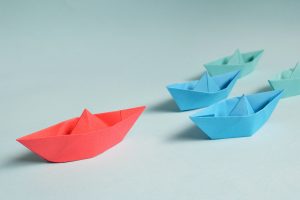 transformational leadership, image of paper boats with one red one leading the blue and green ones.